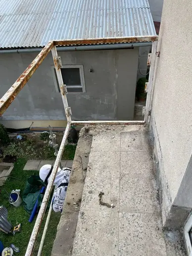 Detail zhora na balkón s poškodenou omietkou a skorodovanou konštrukciou pred opravou a zateplením v Hlohovci.