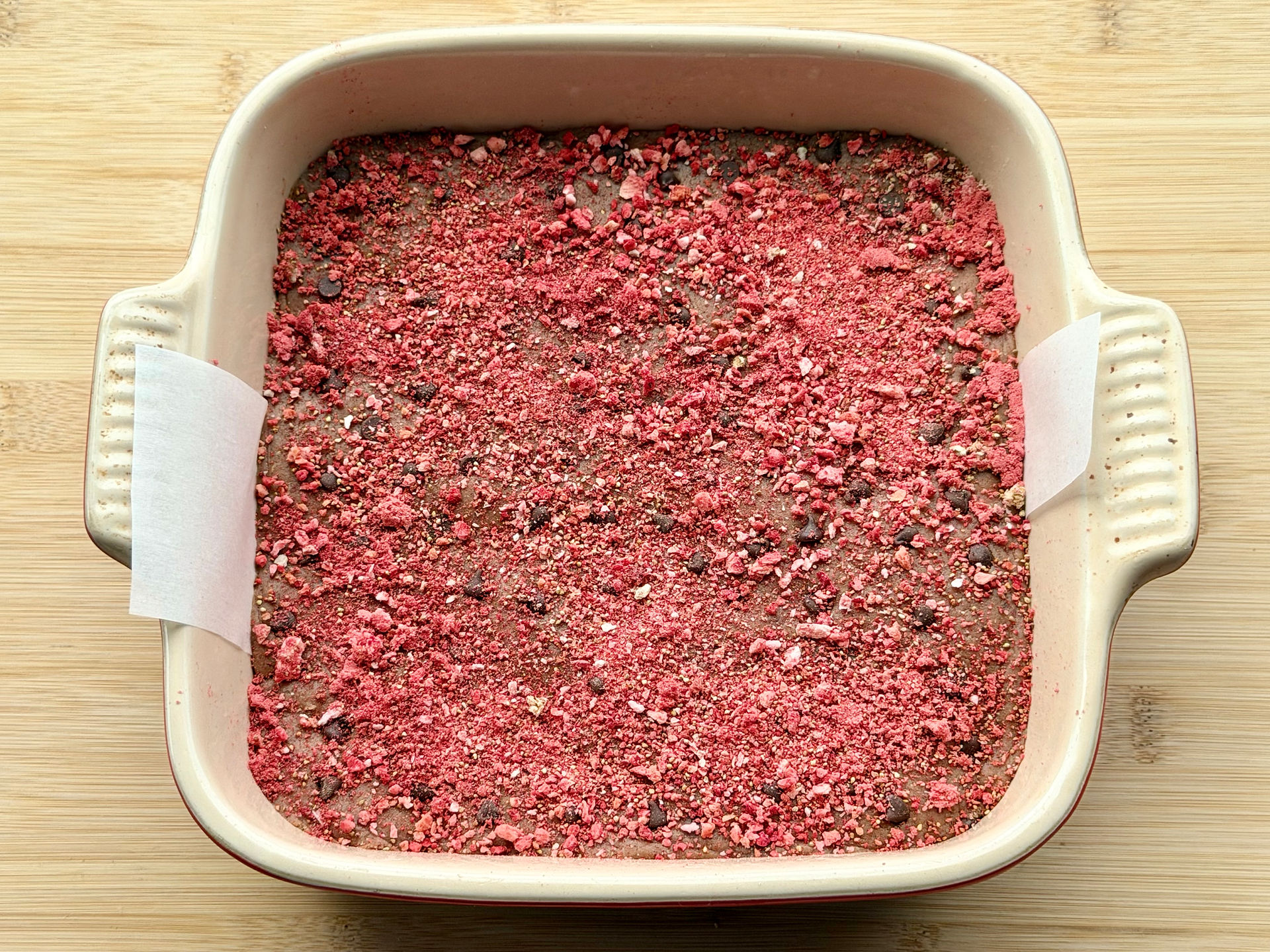 Freeze dried strawberries on top of No-Bake Chocolate Chip PB&J Protein Bar dough in an 8x8 pan