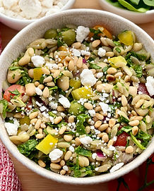 Gluten-Free Cassava Orzo Pasta Salad in a bowl next to a red dish towel, a bowl of feta and tomatoes