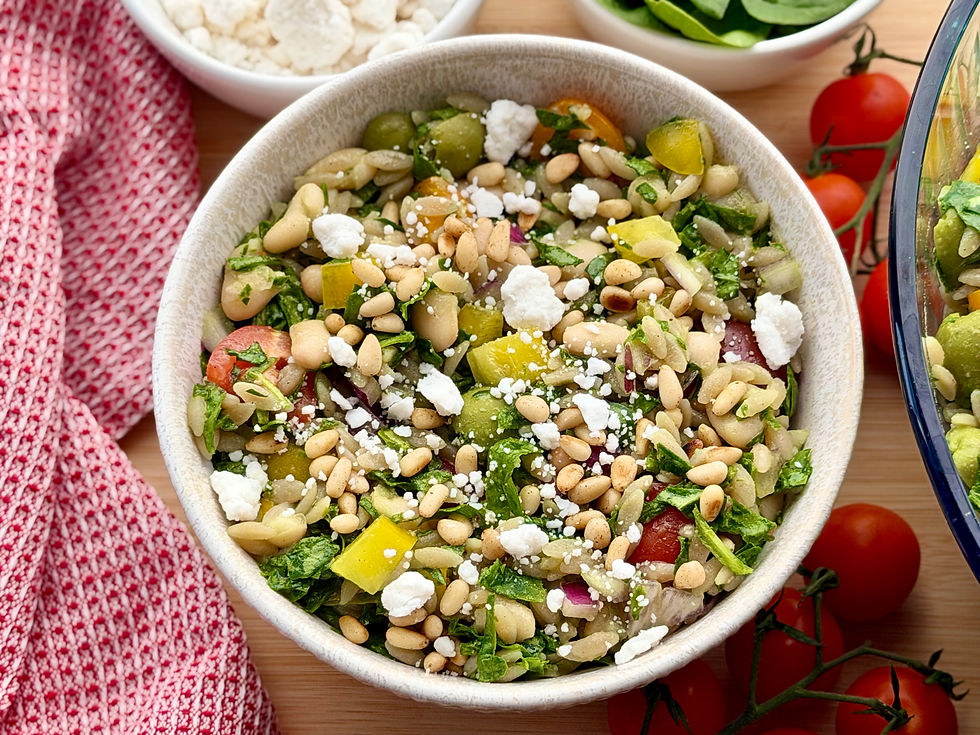 Top view of a Cassava Orzo Pasta Salad with beans, feta, pine nuts, greens, and tomatoes on a wooden table with red cloth and cherry tomatoes