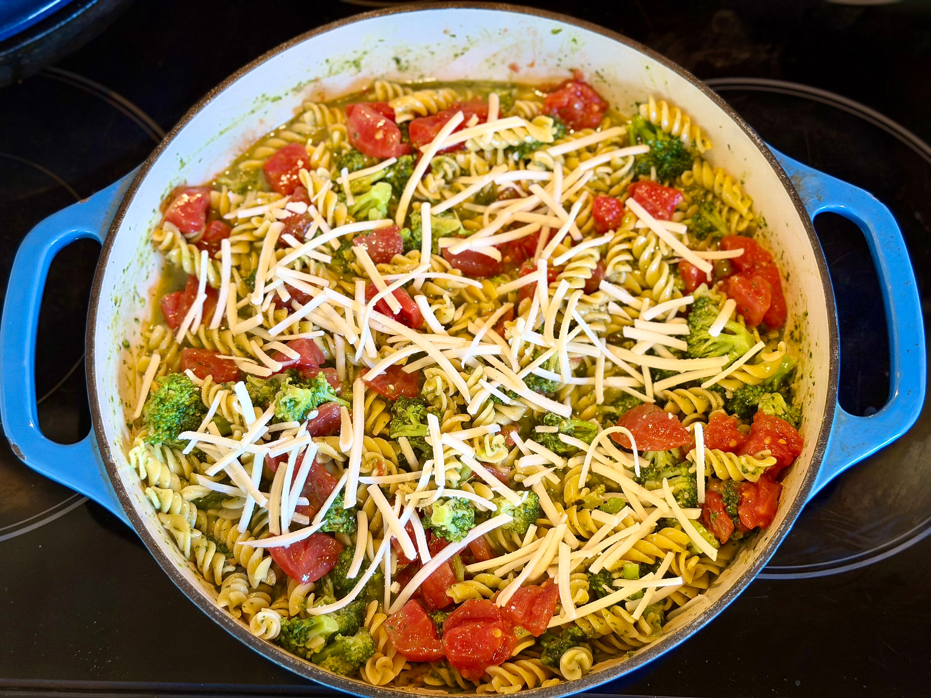 Shredded dairy-free mozzarella cheese scattered evenly across a one-pot gluten-free pesto pasta