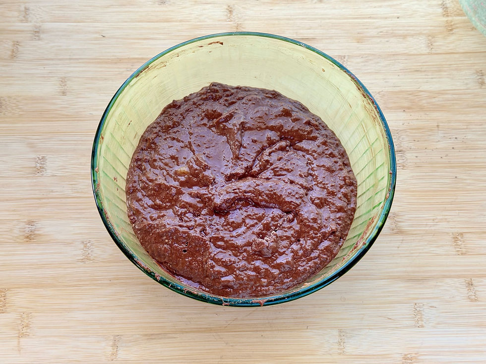 Top view of a glass bowl filled with Gluten-Free Double Chocolate Banana Bread batter on a wooden cutting board