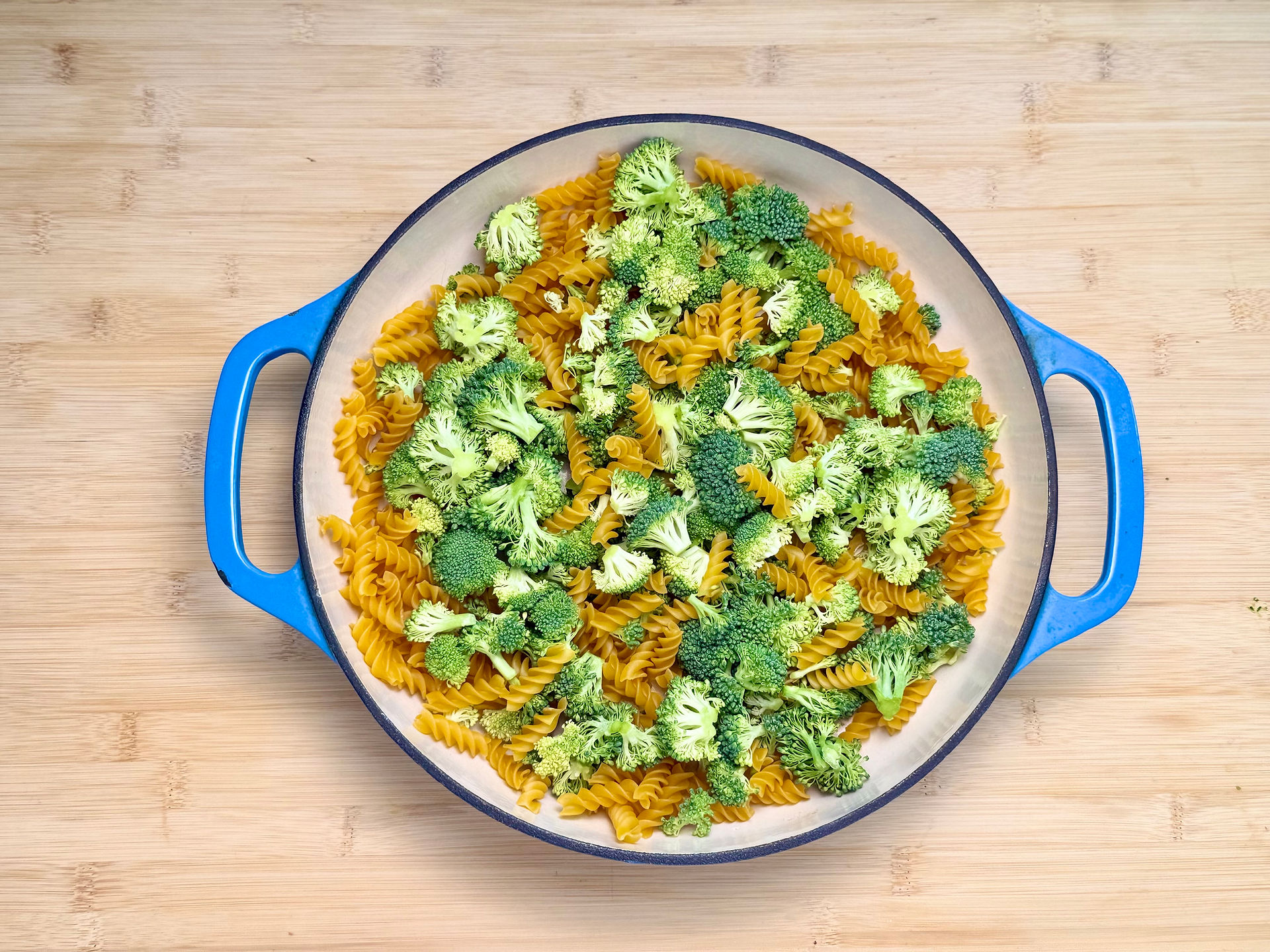 A top-down view of uncooked gluten-free rotini pasta and fresh broccoli florets arranged in a dish 