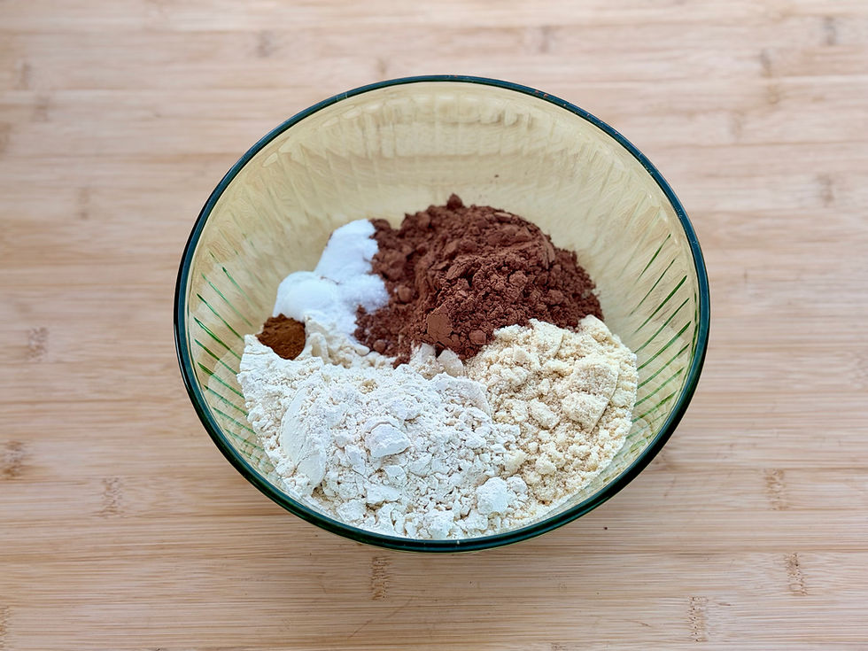 Glass bowl of dry baking ingredients for Gluten-Free Double Chocolate Banana Bread, including flour and cocoa powder, on a wooden countertop.