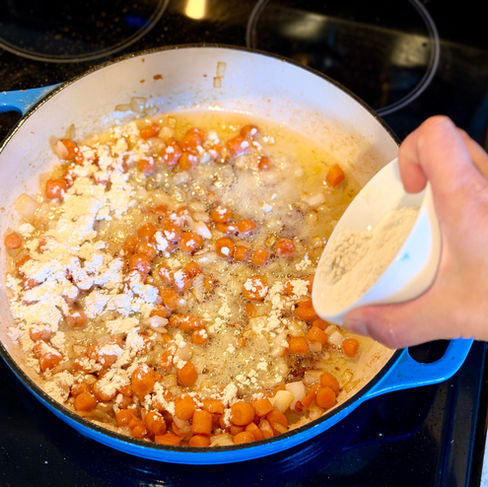 gluten free flour being added to carrots, onions and coconut oil