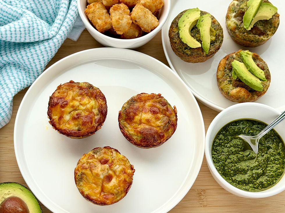 Crispy tater tot egg cups topped with melted cheese and sliced avocado on white plates next to a bowl of fresh basil pesto.