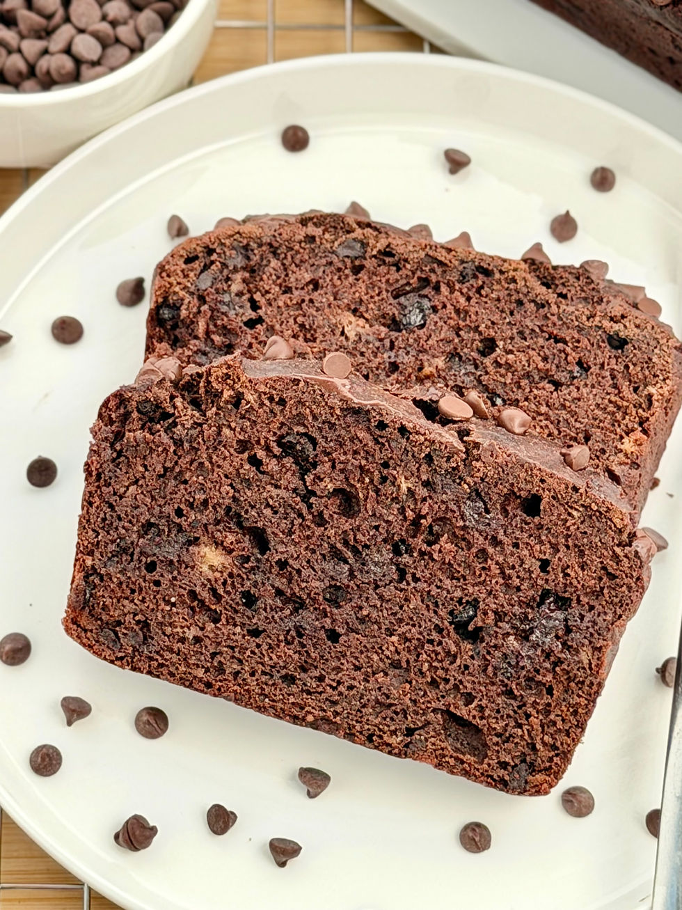 Two slices of Gluten-Free Double Chocolate Banana Bread on a white plate, with chips scattered around on a wooden surface.