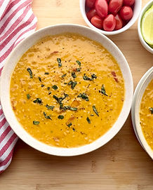 A bowl of curry red lentil soup, sprinkled with fresh herbs, next to a red dish towel, and a second bowl of soup.