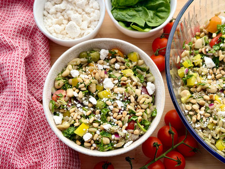 a bowl of orzo pasta salad on a table with tomatoes