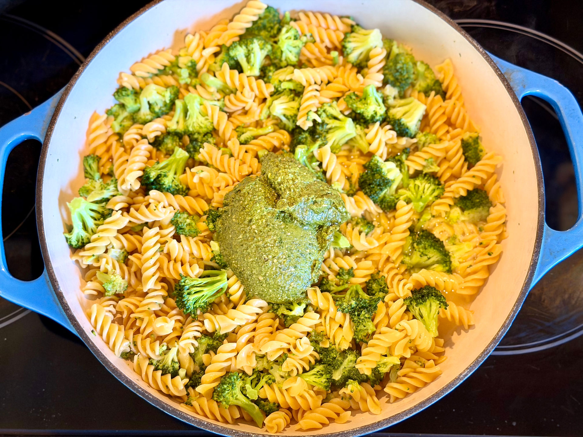 A top-down shot of a large scoop of green vegan pesto sitting in the center of noodles and broccoli