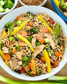 White bowl filled with Gluten Free Chicken Chow Mein loaded with yellow bell peppers, broccoli florets, sliced carrots, snap peas, green onions, and sesame seeds.