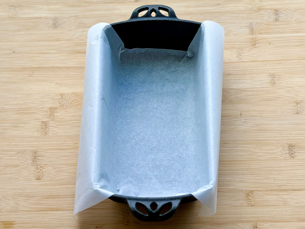 Empty cast iron loaf pan lined with parchment paper on a wooden cutting board, ready for baking.