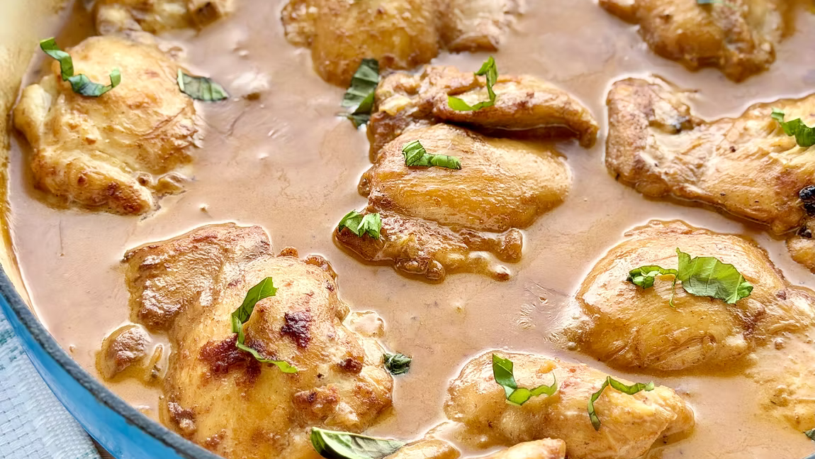 Seared chicken thighs in a rich, creamy pan sauce topped with fresh basil leaves, served in a blue cast-iron skillet.