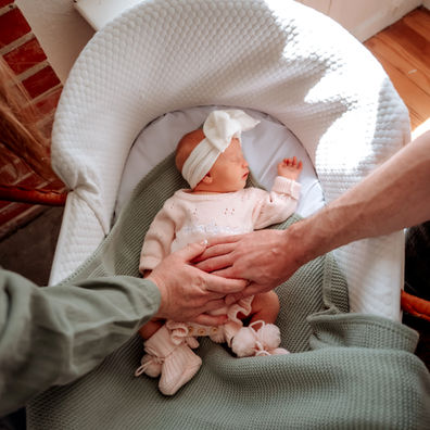 Newborn sleeping in basket, parents holding hands over her