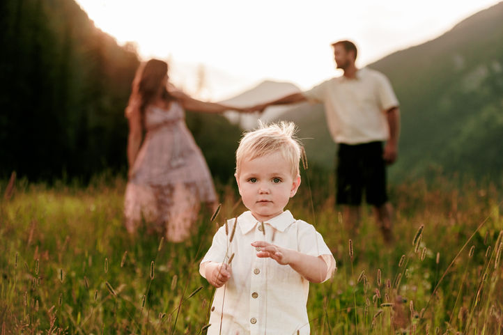 a mother and father dance in the sunset light while a toddler plays