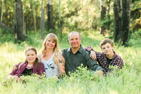 a family poses for photos in tall grass in golden summer light in sparwood