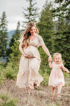A pregnant mother runs through a field with her toddler