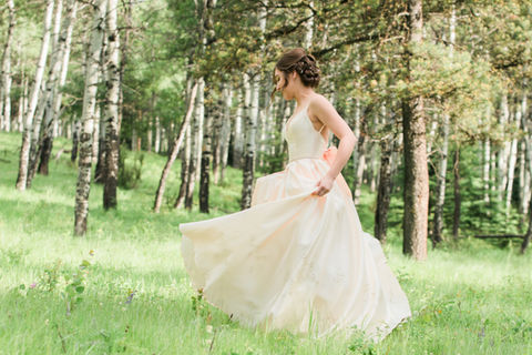 A girl in a white grad gown spins around a mountain meadow in Fernie BC