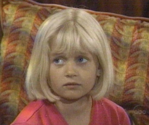 A young Serena Baldwin sits on a couch in a scene from General Hospital.