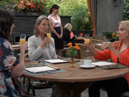 Willow, Nina, and Liesl sit at an outdoor café table on General Hospital, each holding a mimosa, mid-conversation with menus and a small vase of orange flowers on the table.