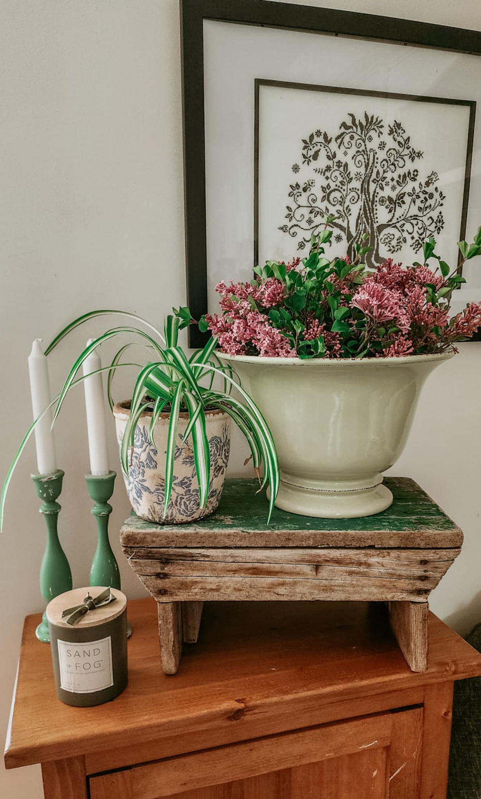 A vignette with candles, a plant, and some fresh cut lilacs.