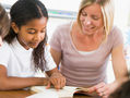 Teaching assistant helping a student read a book.