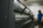 Person in blue shirt operates large industrial wallcovering printer in a brightly lit room. Printer covers have transparent sections, showing internal parts.