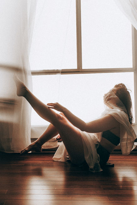 woman in boudoir sitting on floor pose, expressive and vonurable. Set by the window in Luminaire Studio in Calgary, Alberta