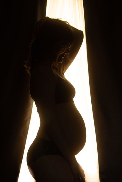 A unique pregnancy boudoir photo from Calgary Boudoir Studio capturing the beauty of maternity glow.  Stunning, elegant and empowering photo of woman posing that highlight her baby belly 