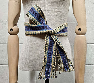 Multicolored hand woven belt tied in a half bow around the waist of a dress form.