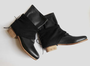 Black leather boots laying together on their sides. The ankle portions are covered by black wool gaiters, which lace closed in the back.