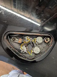 Open electronics cavity of an electric guitar showing wiring and control pots during electrical servicing