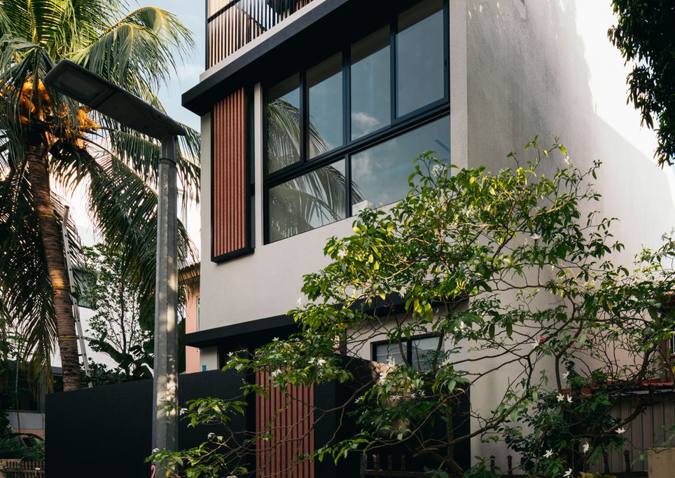 Side exterior view of a modern multi-story home showcasing large glass windows, white exterior cladding, and surrounding tropical foliage.