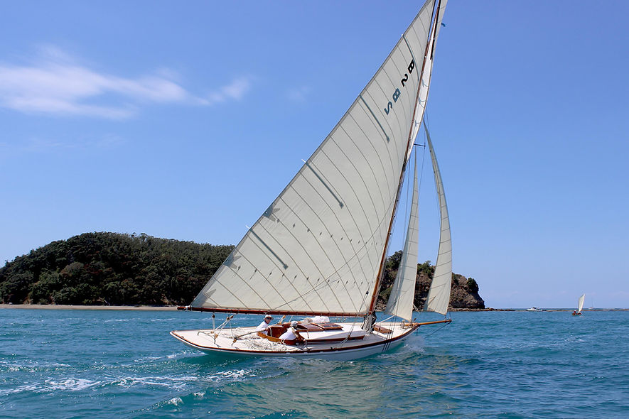 Elegant classic sloop sailboat with a large mainsail, sailing in a scenic coastal area.