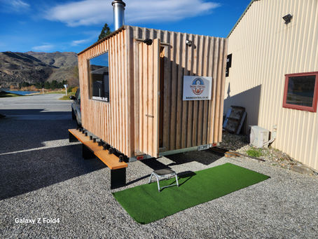 The exterior of a mobile sauna trailer by Sauna Central with a panoramic window and a view of mountains in Cromwell, New Zealand.