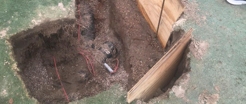 Excavated trench exposing a drainage pipe beneath a stressed golf green