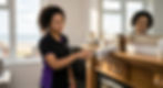 A close-up photograph of a professional cleaner from Spify, wearing the black and purple branded uniform, diligently dusting an ornate wooden mantlepiece. Sunlight illuminates fine dust particles in the air and on the surface, emphasizing the cleaning action. The background shows a clean, modern living room and a soft view of the Bridlington coastline through a large window.