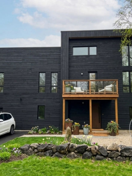 A large, modern two-story home with flat rooflines entirely clad in black textured wood siding.