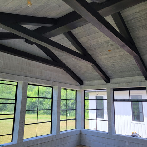 Modern interior with a vaulted wood ceiling, dark timber beams, and large industrial-style windows.