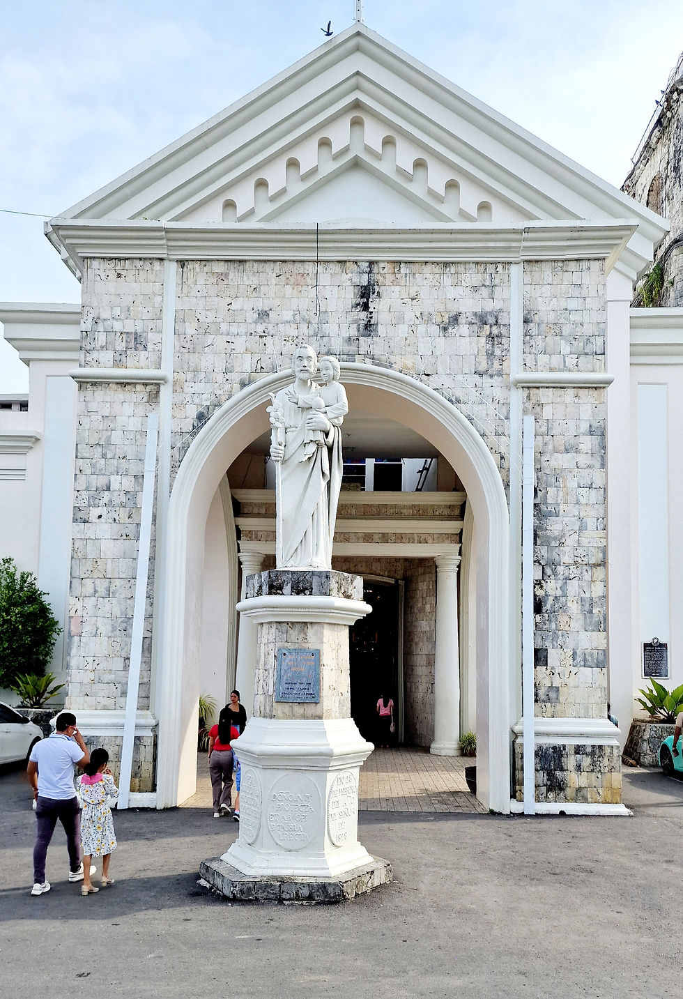 The portal of the gleaming white church is shining and believers are on their way into the church. In front of it you can see a monument.