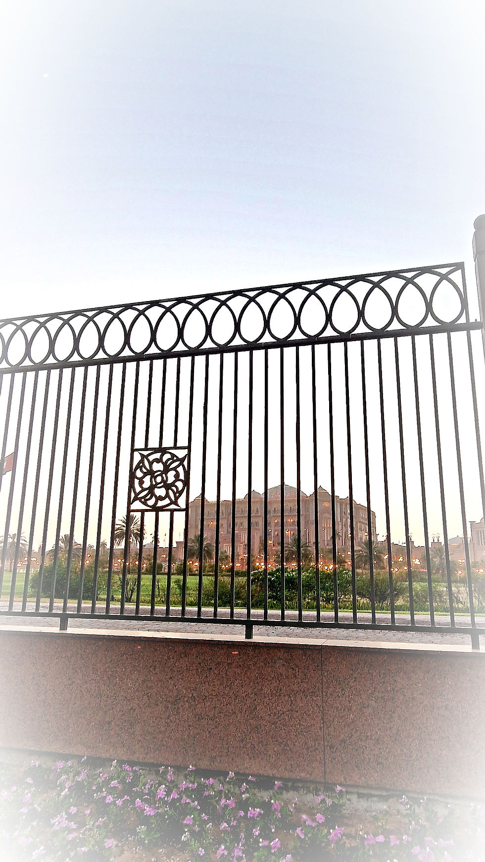 Behind large metal grilles, in the middle of the extensive park, lies the Emirates Palace Hotel Abu Dhabi.