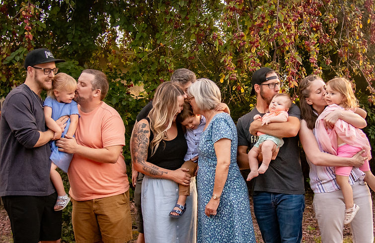 Large family poses embracing, smiling, and kissing outdoors for a portrait.