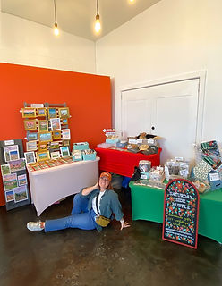 Woman poses at a colorful market display with various products and signs.