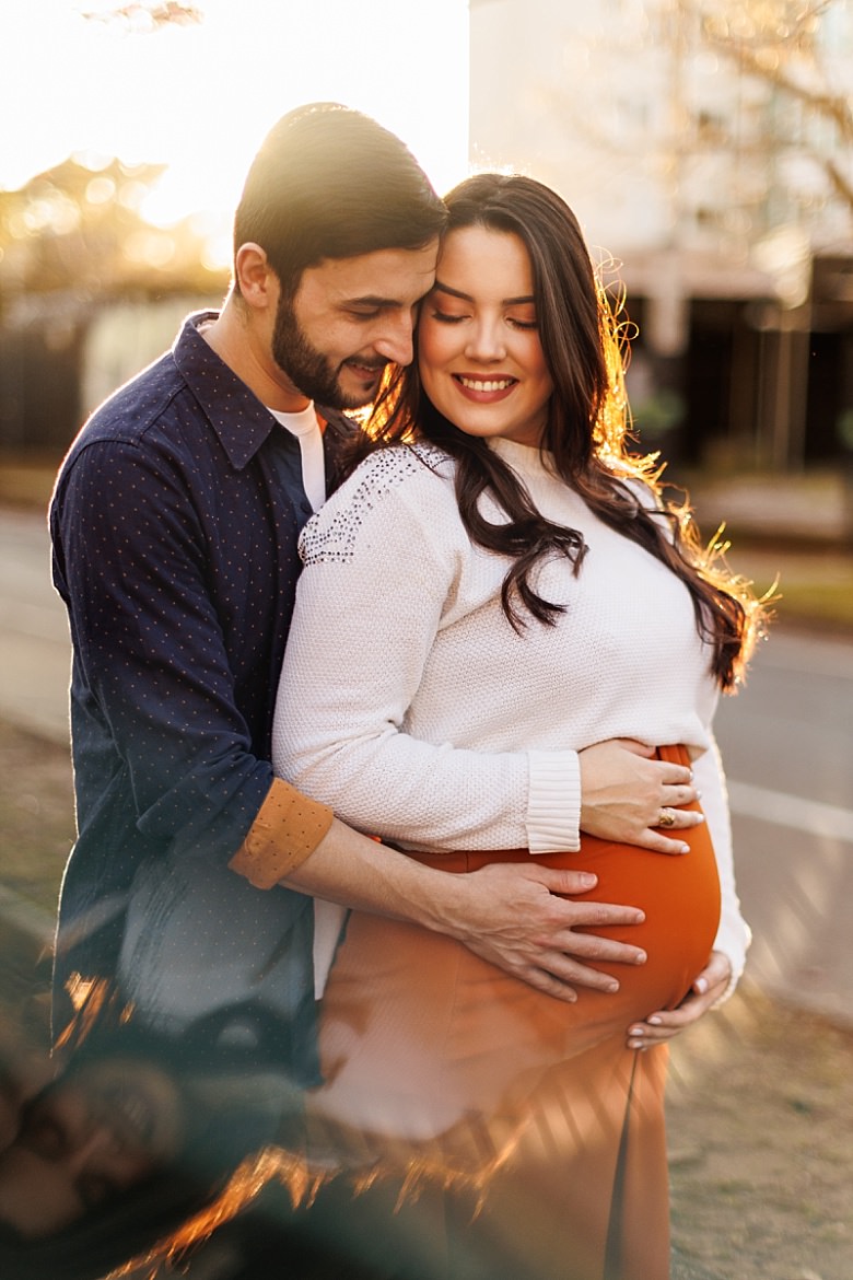 Casal ao pôr do sol posando para ensaio fotográfico de gestante