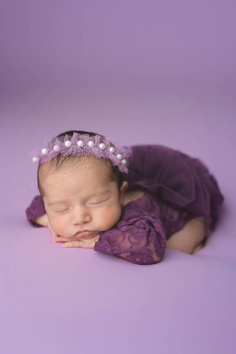 Newborn at 16 days posing in our studio in Aurora, CO. She is wearing a gorgeous lace romper with fluffy tulle and a light purple lavender pearl headband. The outfit was provided by our studio.