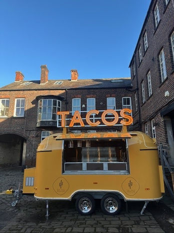 Yellow taco trailer with 'TACOS' sign in a brick courtyard