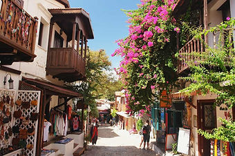 View of a narrow street in the Old Town of Kaş, featuring stone-paved paths and colorful bougainvillea under a clear sky.
