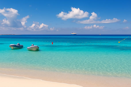 Sandy beach with sailing yachts and catamarans anchored offshore in Formentera.