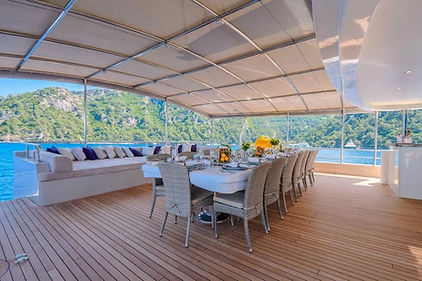 Expansive aft deck of yacht King of the Sea, showing the seamless transition from the elegant main salon to the alfresco dining area and a grand full-beam sofa with plush cushions.