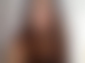 A woman with long brown hair smiles in a gray tank top. She stands in front of a white door, creating a casual and relaxed mood.